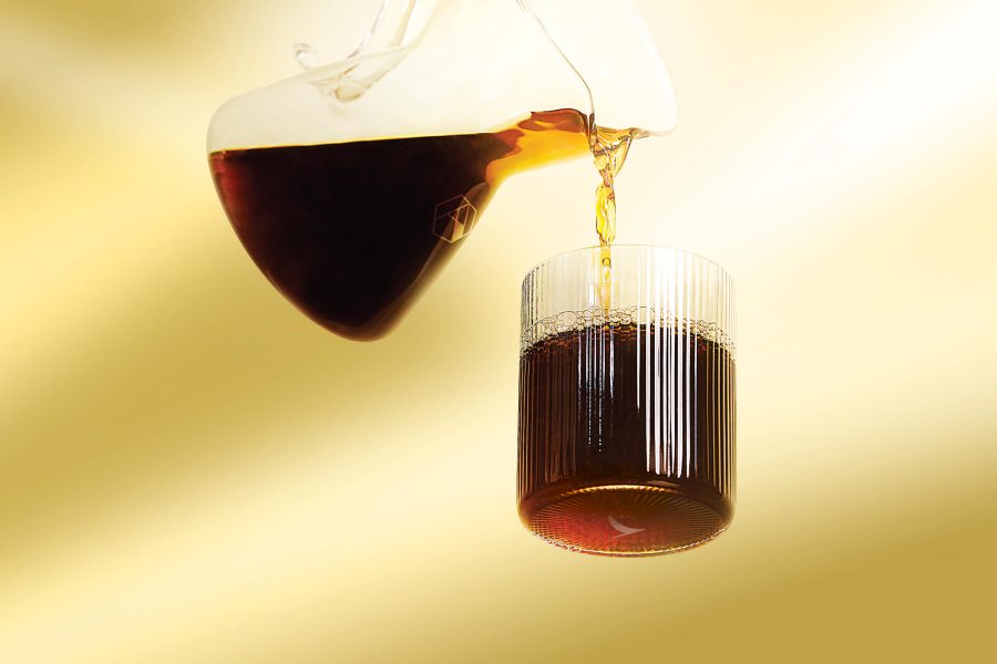 Kopi hitam dituangkan dari pitcher kaca ke dalam gelas bening bergaris dengan latar belakang kuning keemasan. 